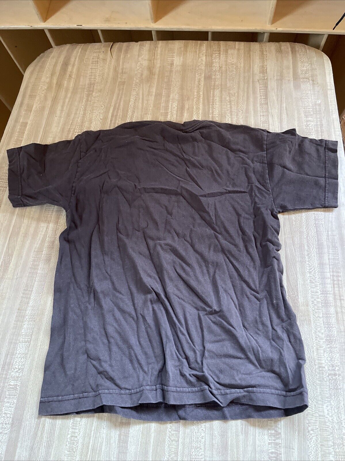 Wrinkled black AAA rock concert shirt large laid flat on beige striped surface