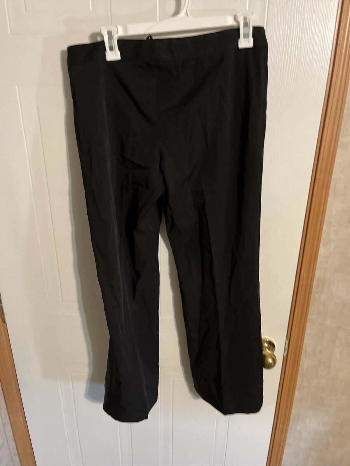 Alyn Paige black pants size 8 hanging on white hanger against white door background