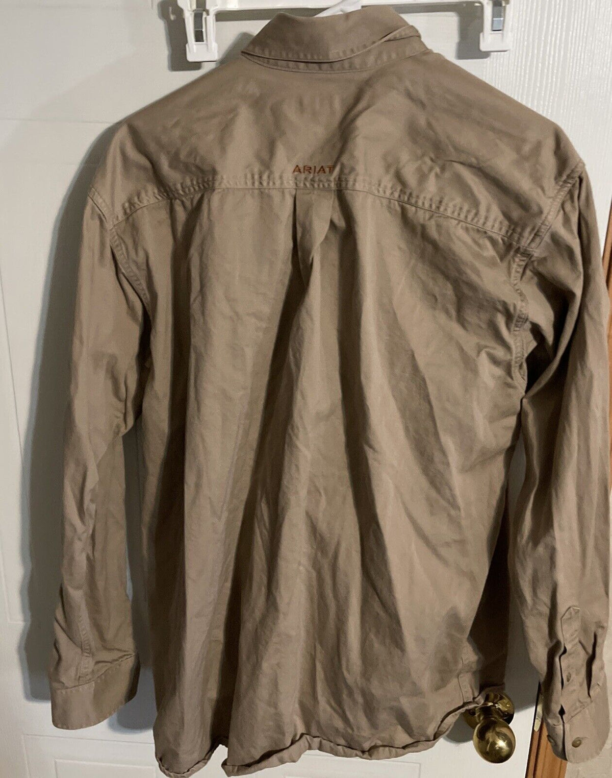 Back view of Ariat men’s button down shirt in light brown with long sleeves hanging on a hanger