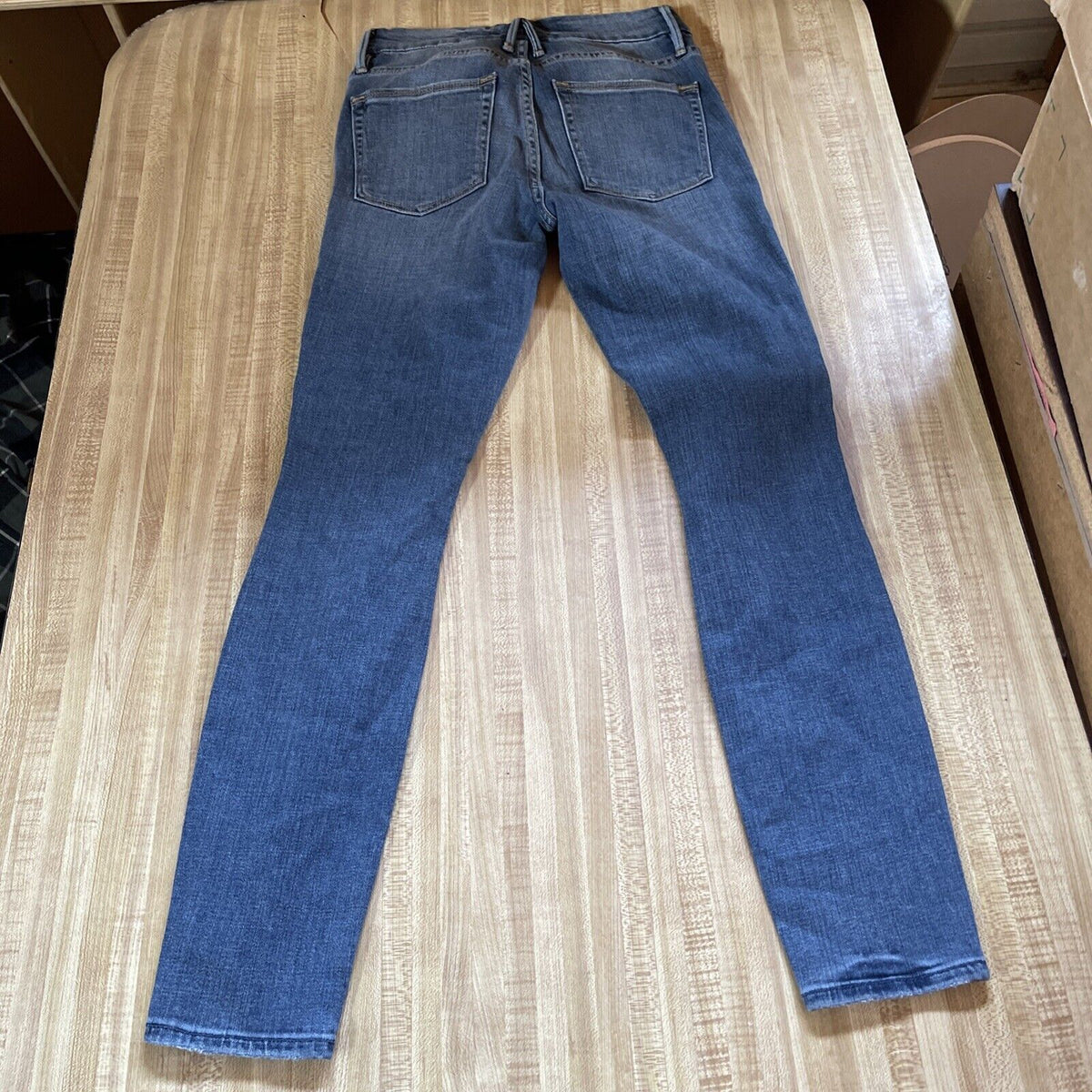 Good American ankle crop jeans in blue denim laid flat showing back pockets and stitching details
