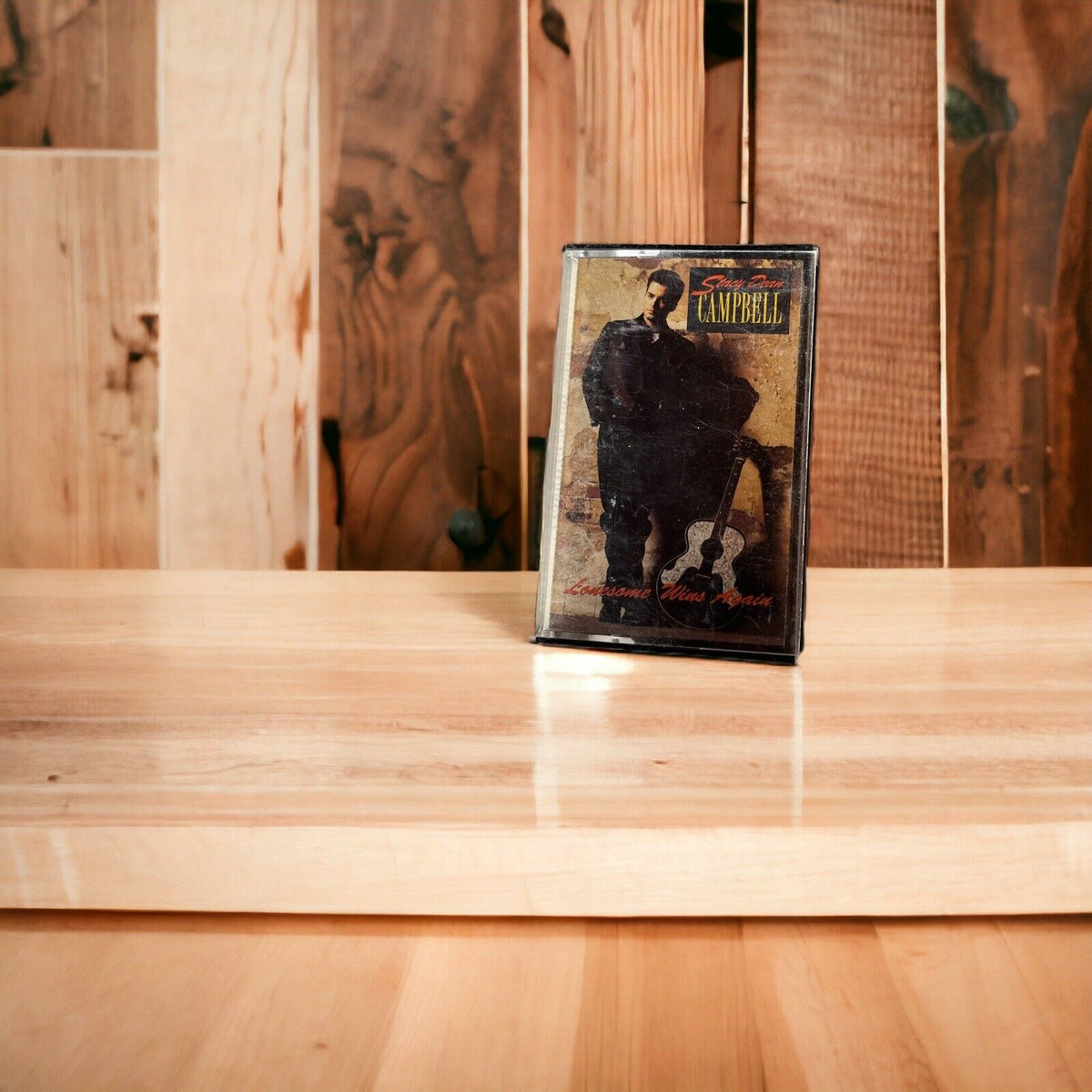 Stacy Dean Campbell Lonesome Wins Again cassette standing on wooden surface with rustic wooden background