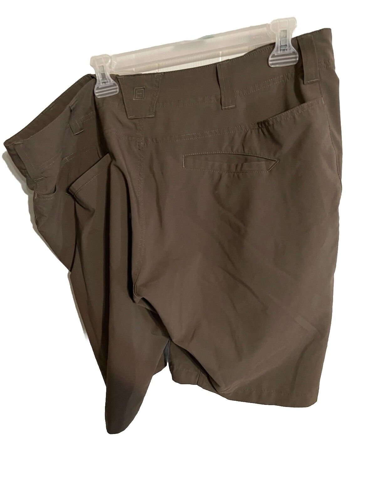 Brown 5.11 tactical shorts for men hanging on clear plastic hanger showcasing back pockets