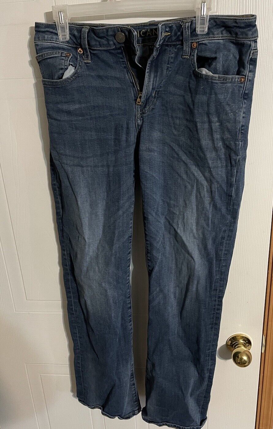 American Eagle bootcut jeans in dark blue denim hanging on a hanger with visible front pockets and button closure