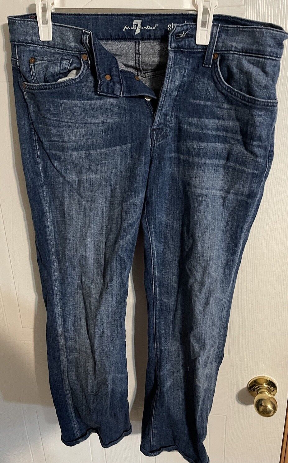 Dark wash 7 for all mankind jeans hanging with front button open showing classic five-pocket design