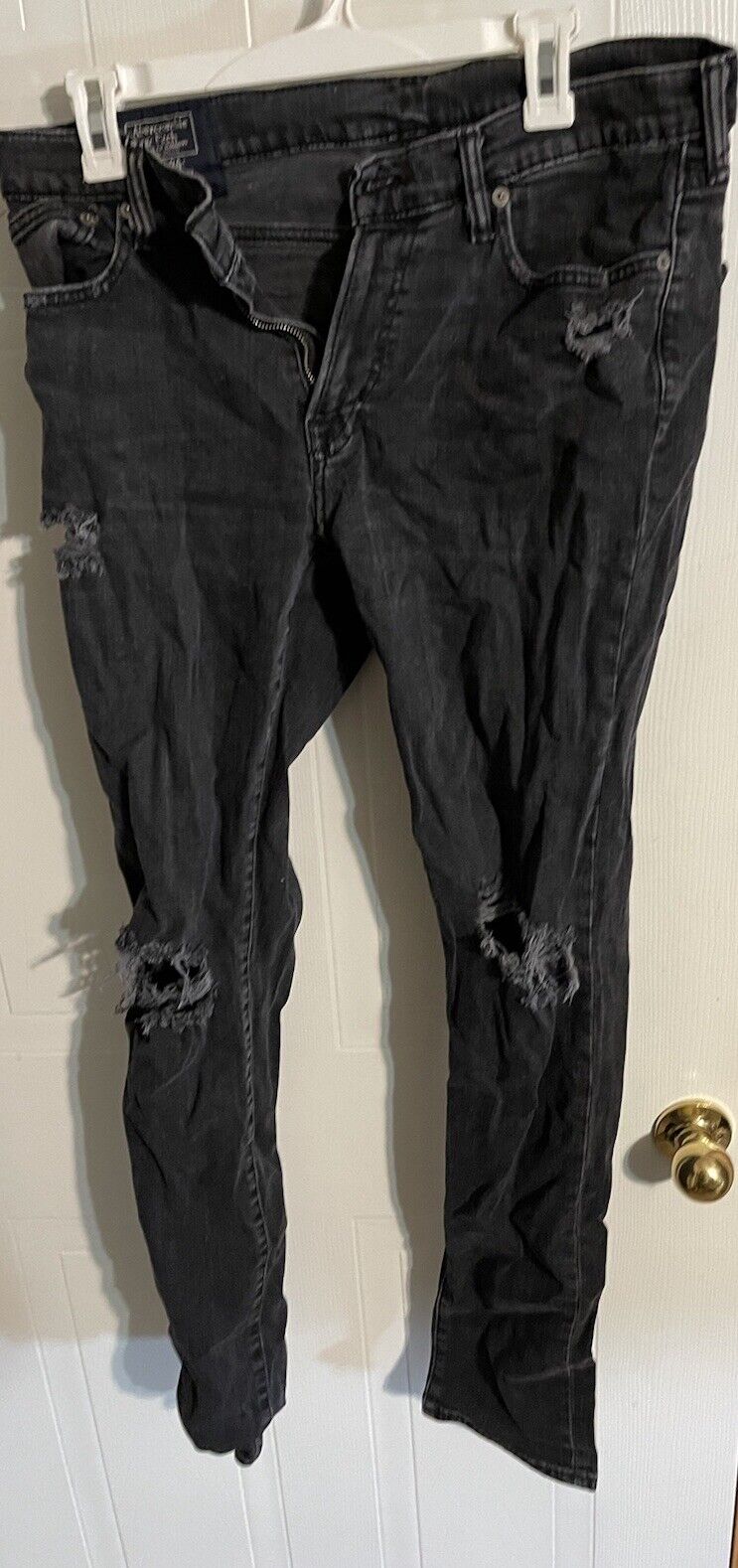 Black distressed Abercrombie Fitch Langdon slim jeans hanging on white hanger with ripped details