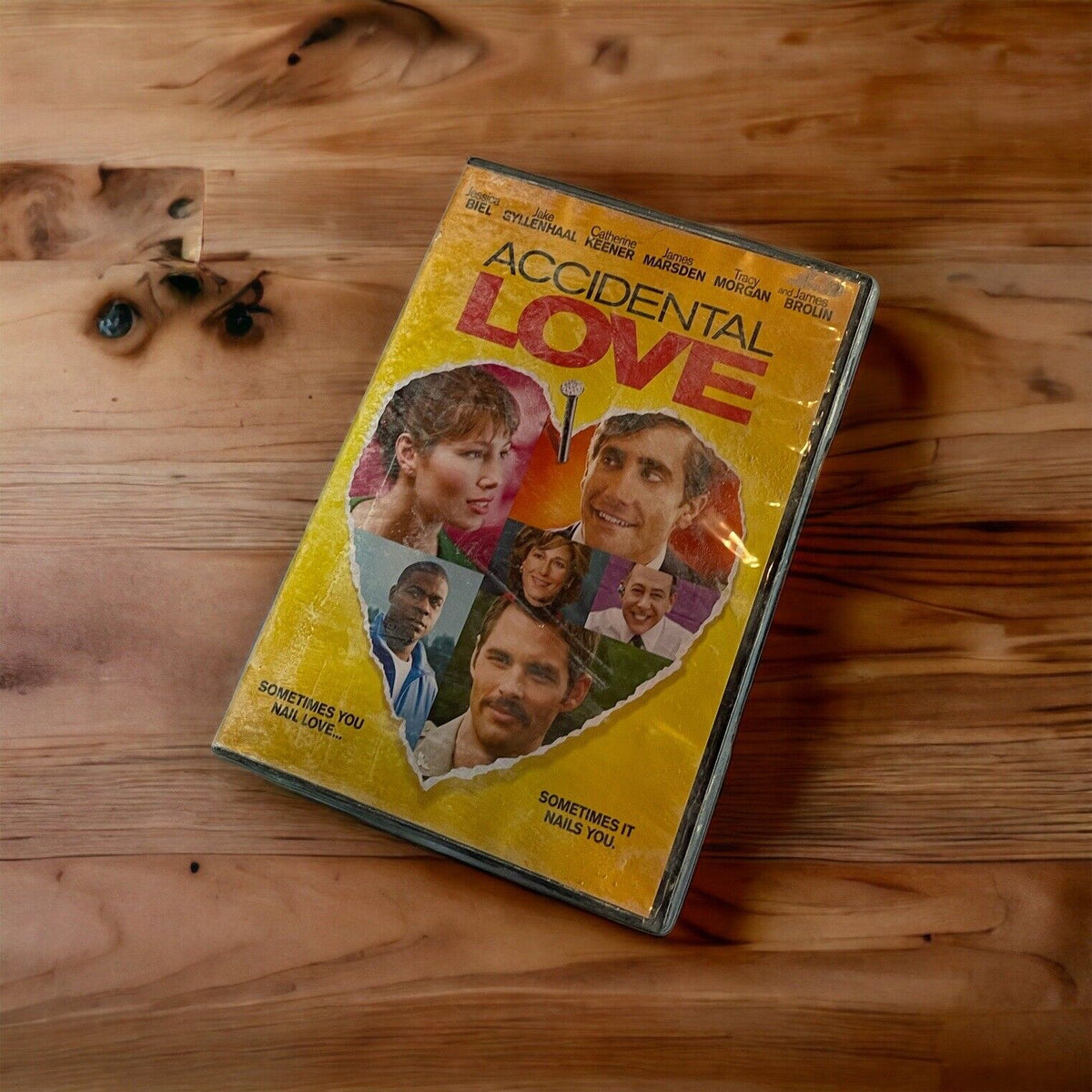Accidental Love DVD with yellow cover featuring a torn heart and cast photos on wooden surface