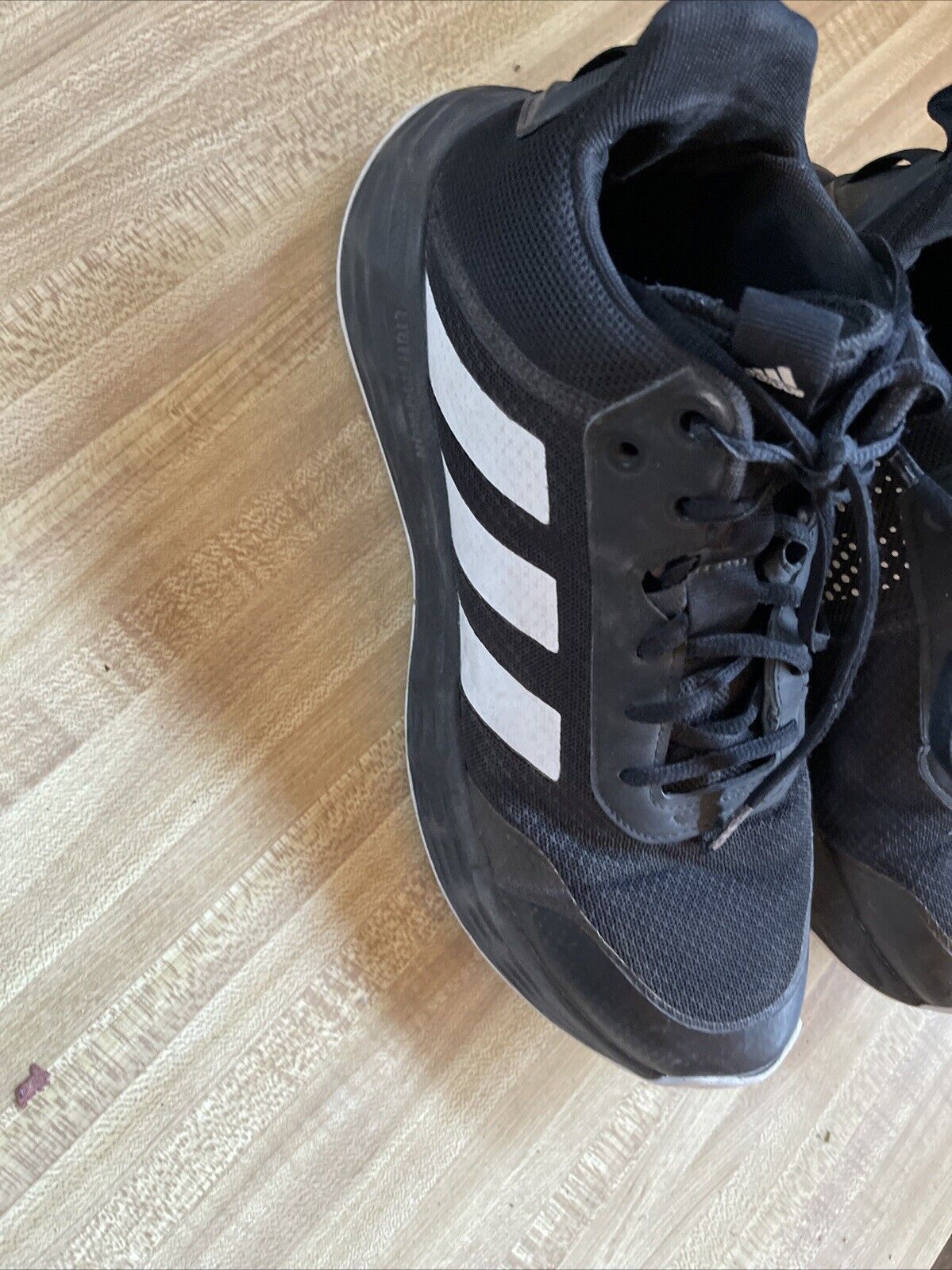 Black adidas lightmotion size 11 running shoes with white stripes on wooden floor