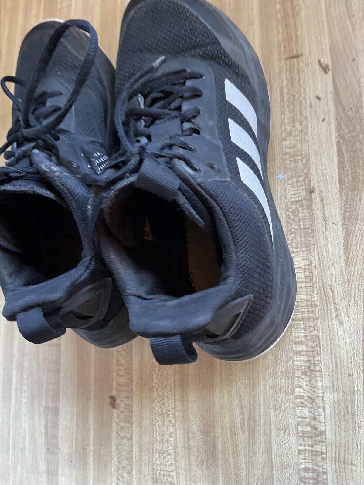 Pair of black adidas lightmotion size 11 running shoes with white stripes on wooden floor