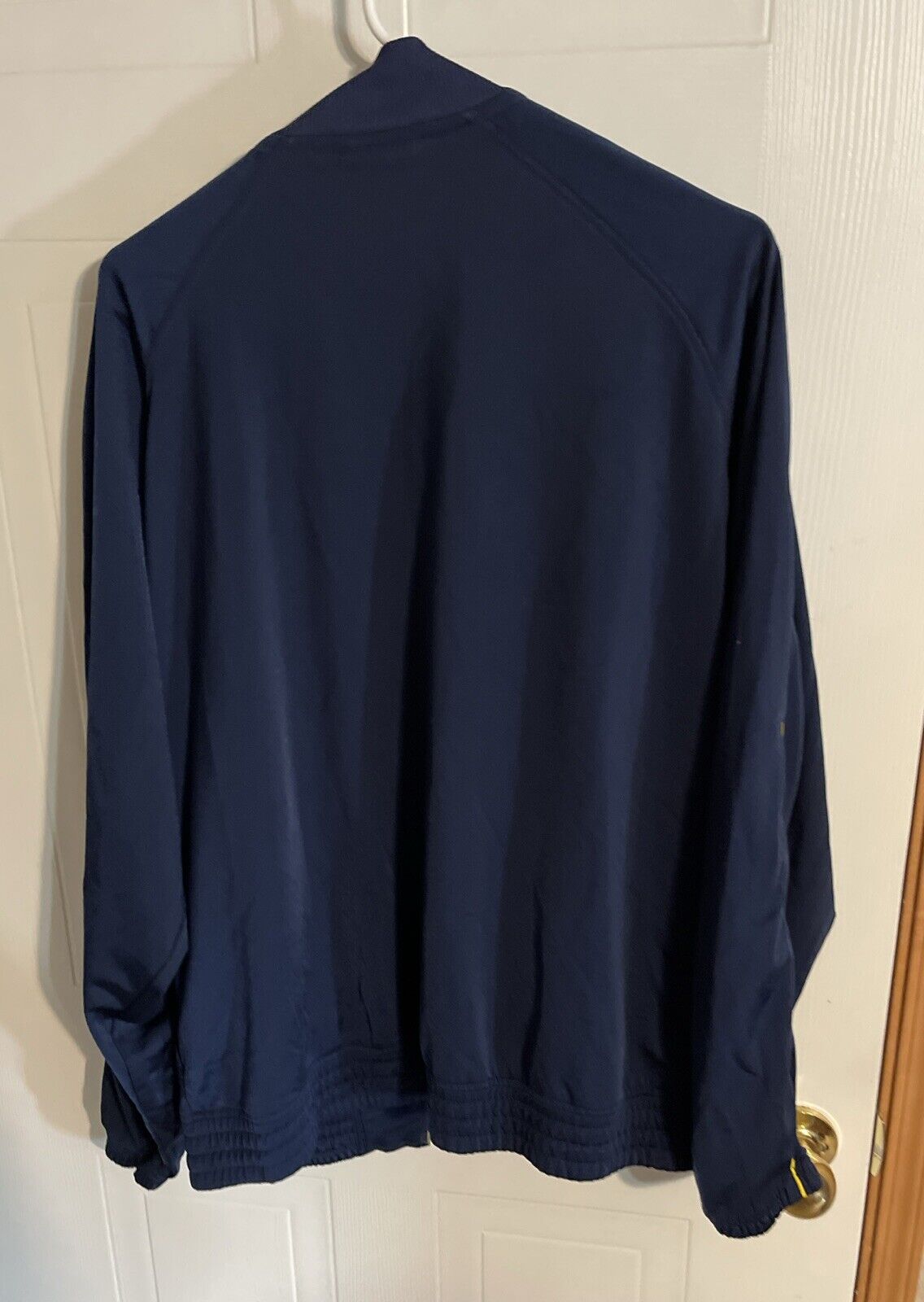 Back view of Adidas track jacket large in navy blue hanging on white door