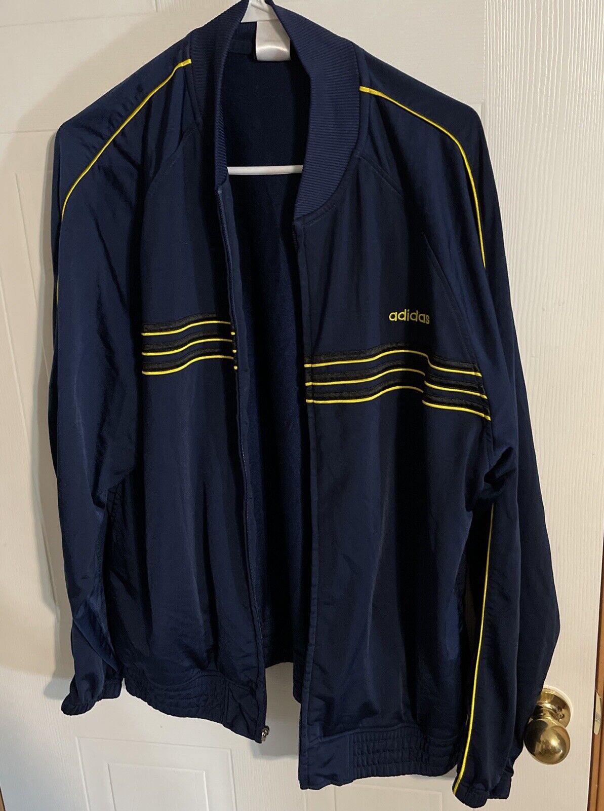 Adidas track jacket large in navy blue with yellow stripes hanging on a white hanger