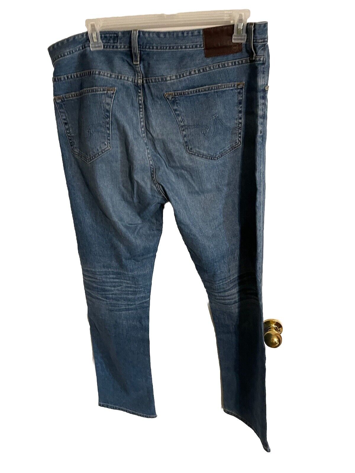 AG Jeans The Ives 38x31 blue denim jeans hanging with back pockets visible and leather patch