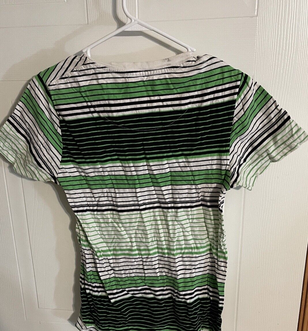 Green, black, and white striped Airwalk V neck T shirt hanging on a white hanger against a white door