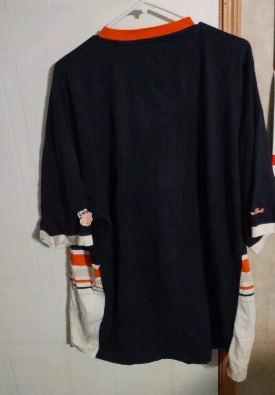Back view of black Akdmks XXL T shirt with orange collar and white striped sleeves hanging on hanger