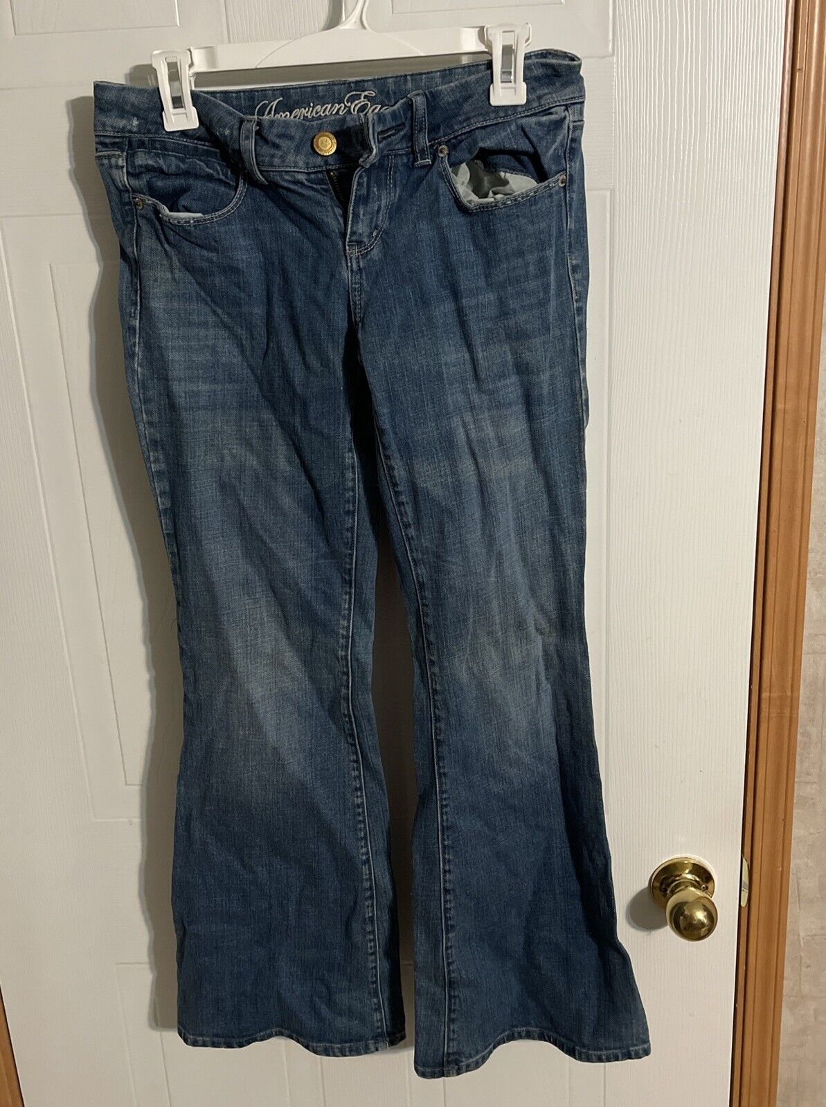 Blue denim American Eagle flare jeans hanging on white hanger against door