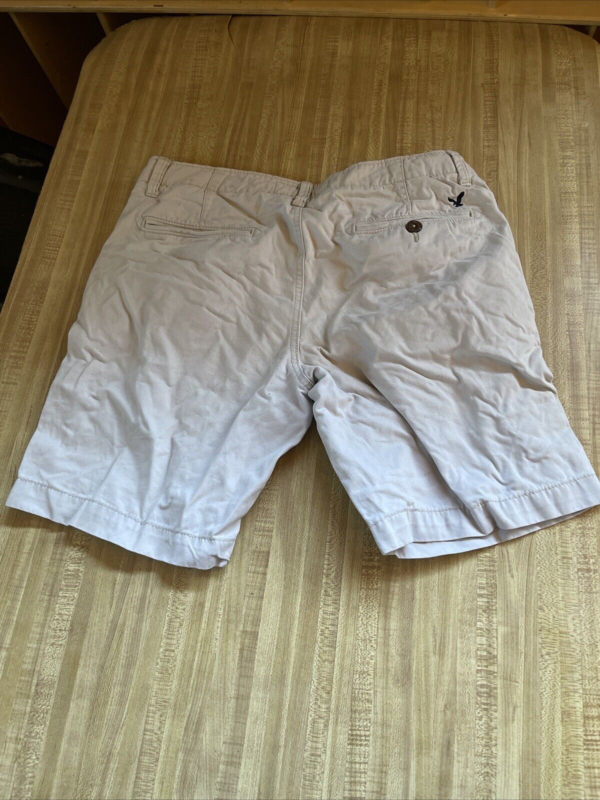 White casual American Eagle shorts 33 with buttoned back pockets laid flat on wooden surface