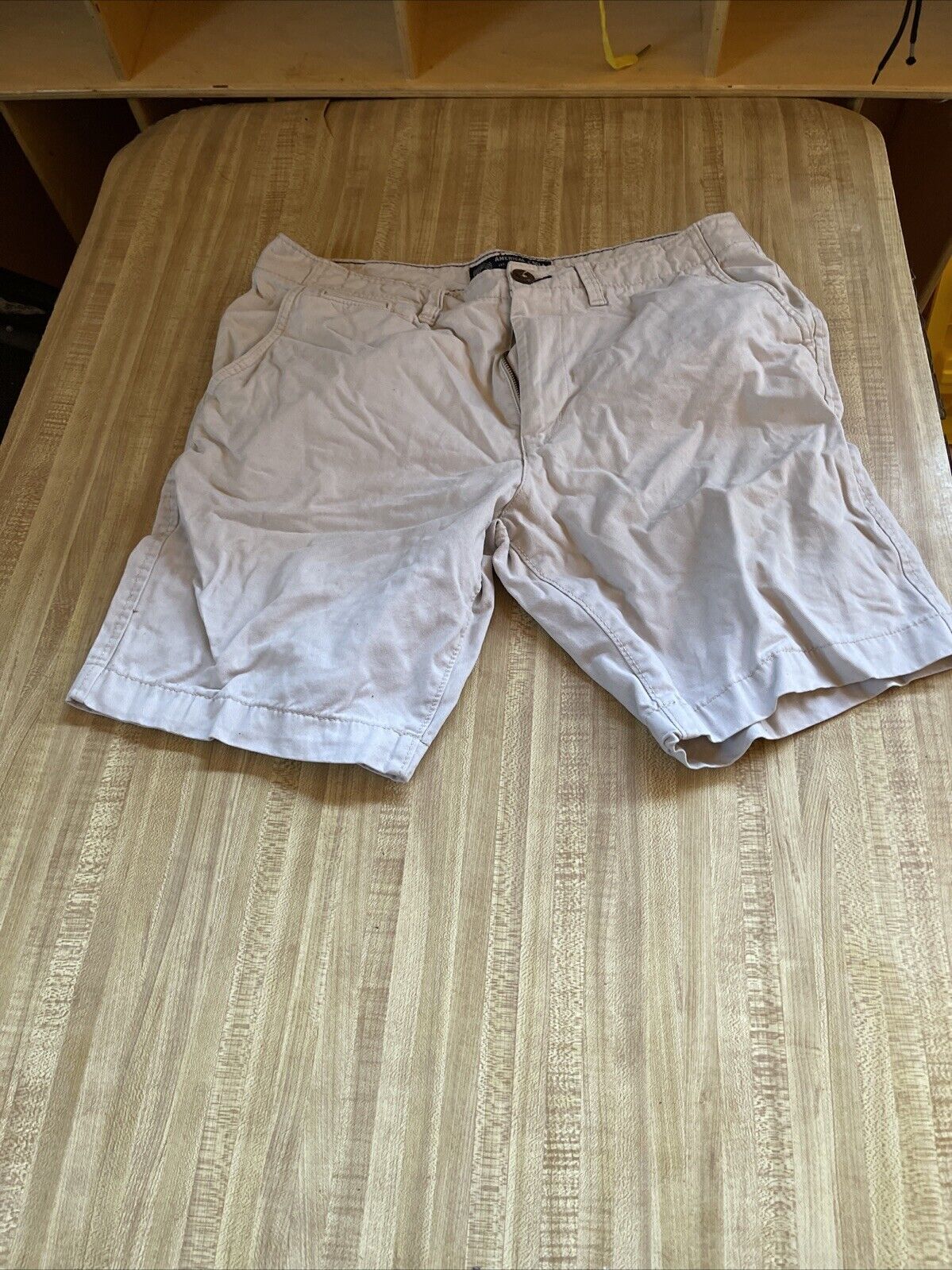 Light beige American Eagle shorts 33 laid flat on a wooden surface with front pockets and button closure