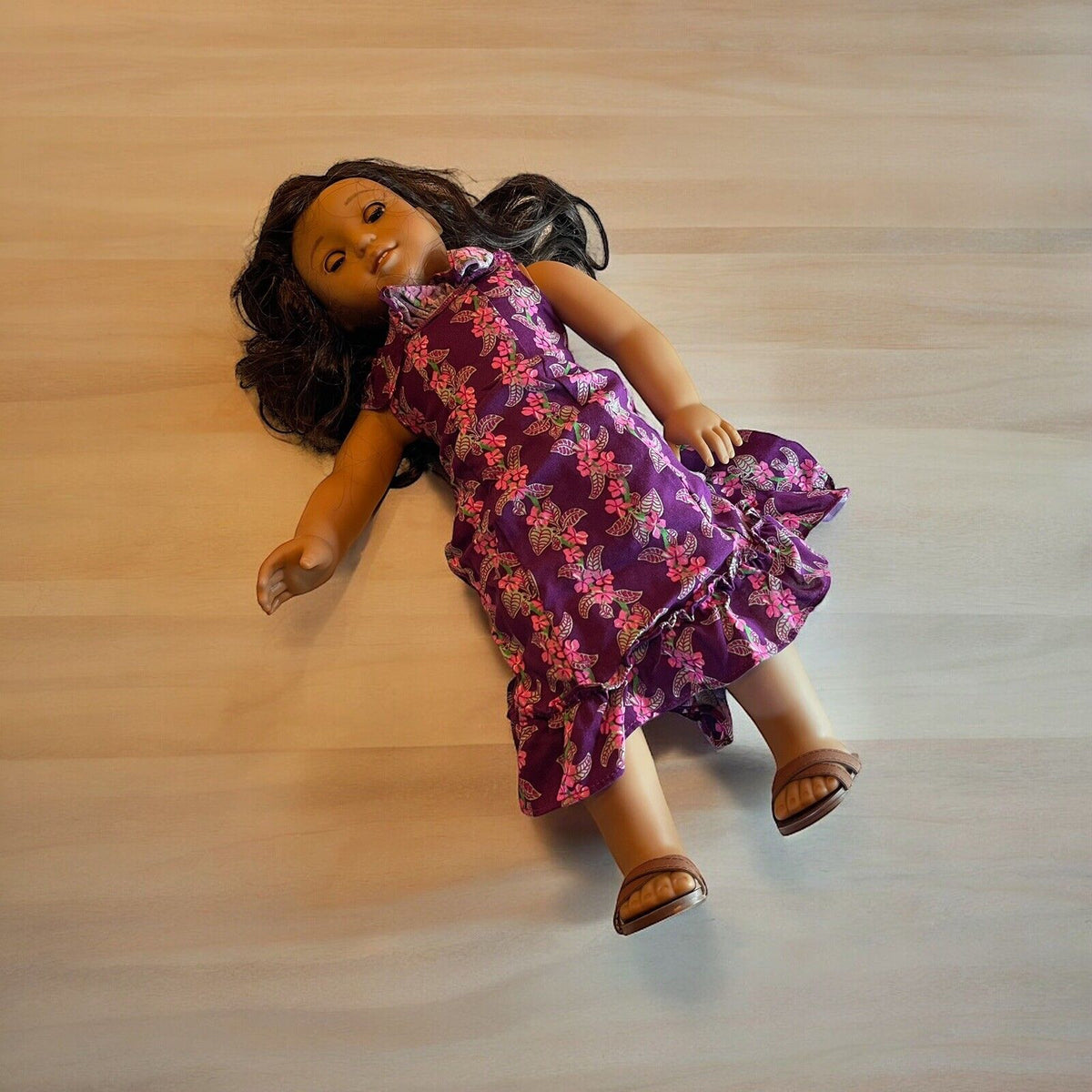 American Girl doll for sale wearing purple floral dress and brown sandals lying on wooden surface