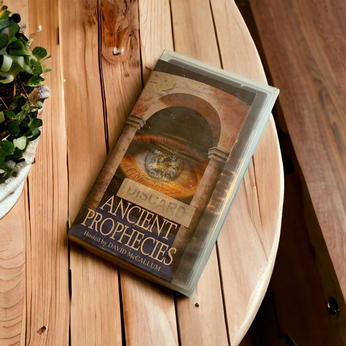 Ancient Prophecies VHS tape with vintage cover art placed on wooden round table near plant