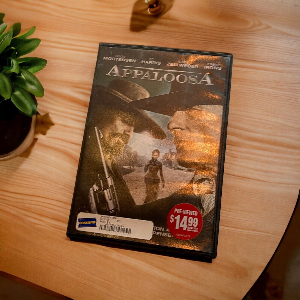 Appaloosa DVD Blockbuster case resting on wooden table next to green potted plant
