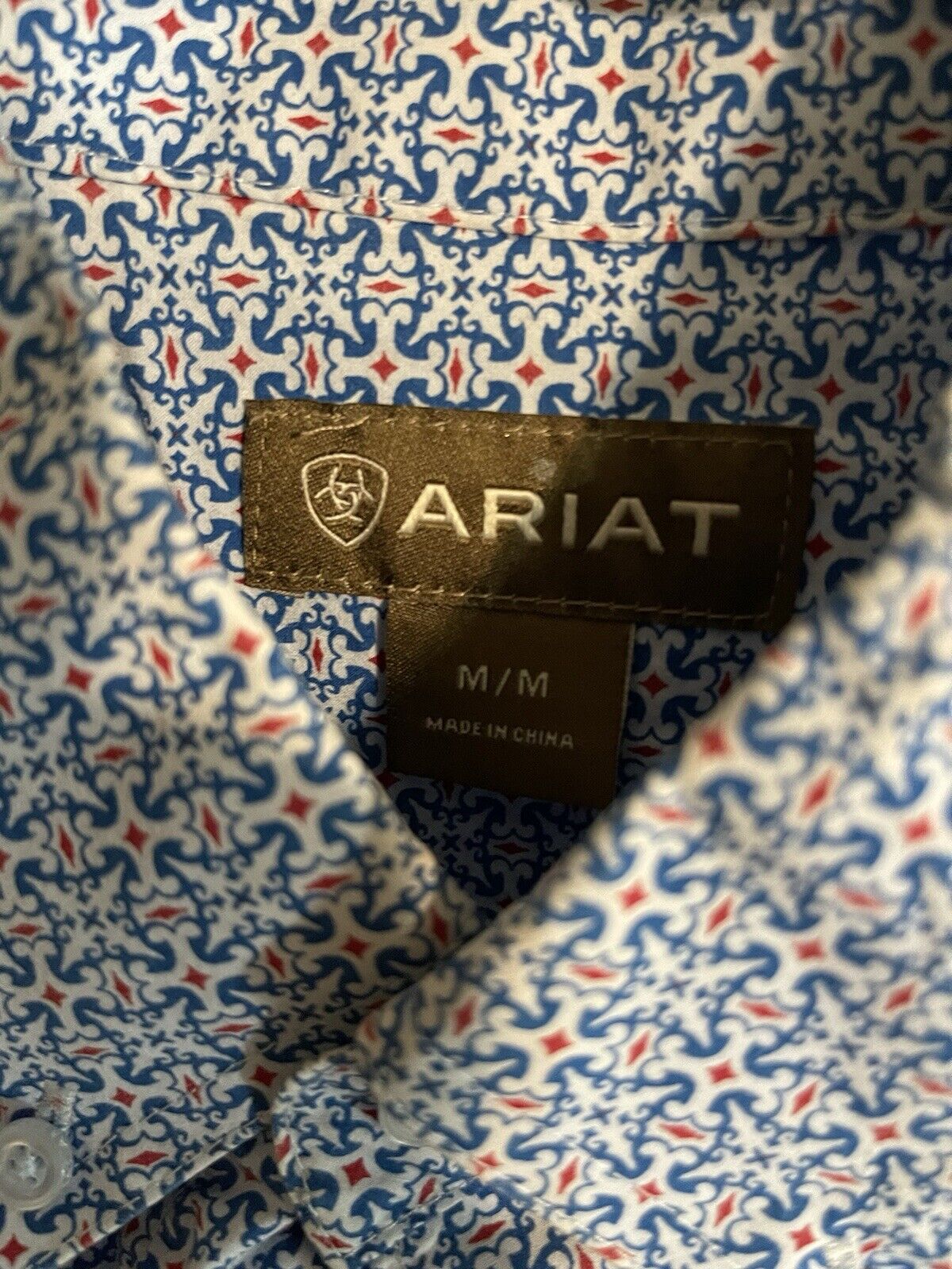 Close-up of Ariat men's button down shirt collar with blue and red patterned fabric and brand label