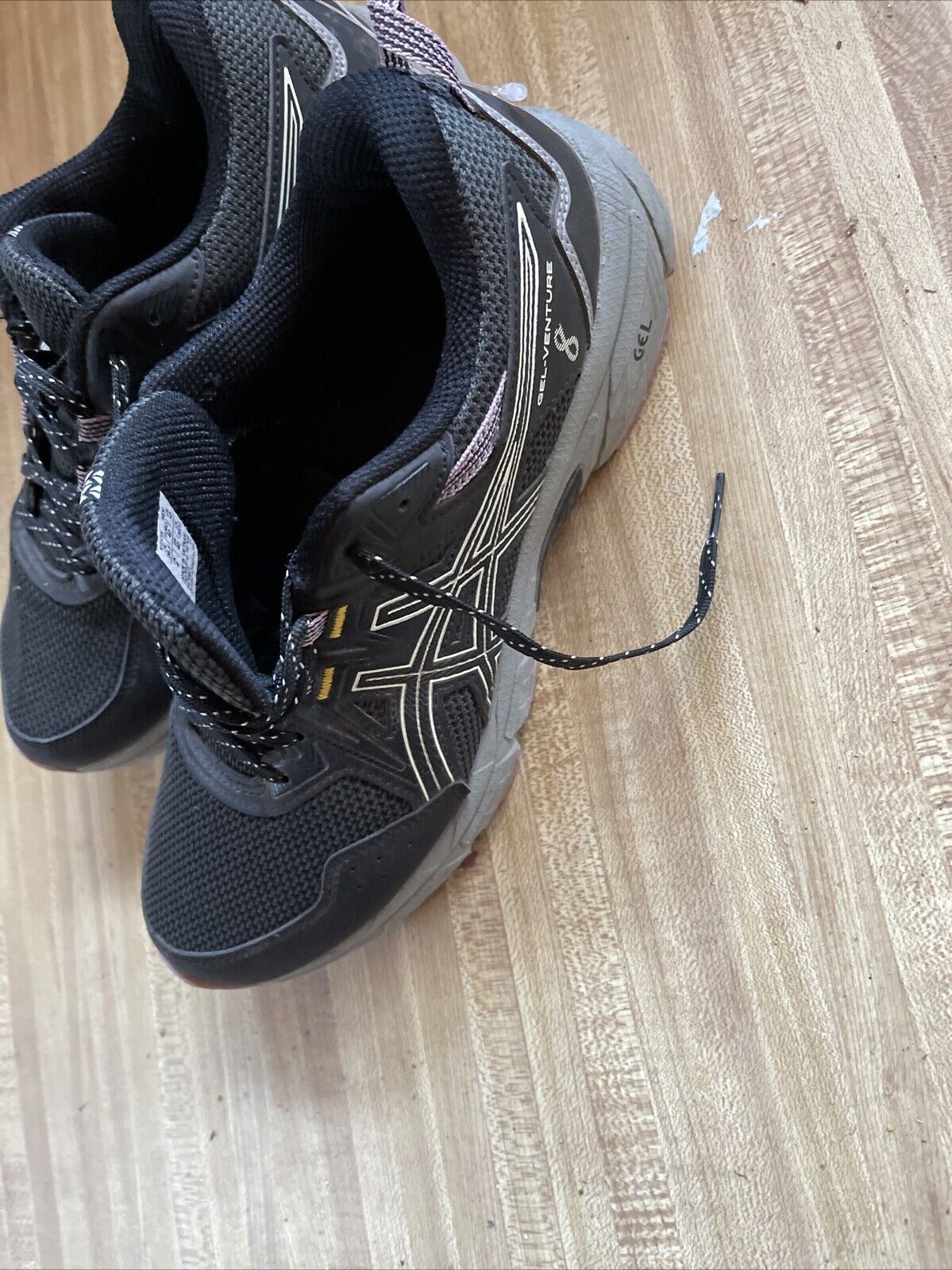 Black ASICS Gel Venture 8 women’s wide running shoes with mesh upper and durable sole on wooden floor