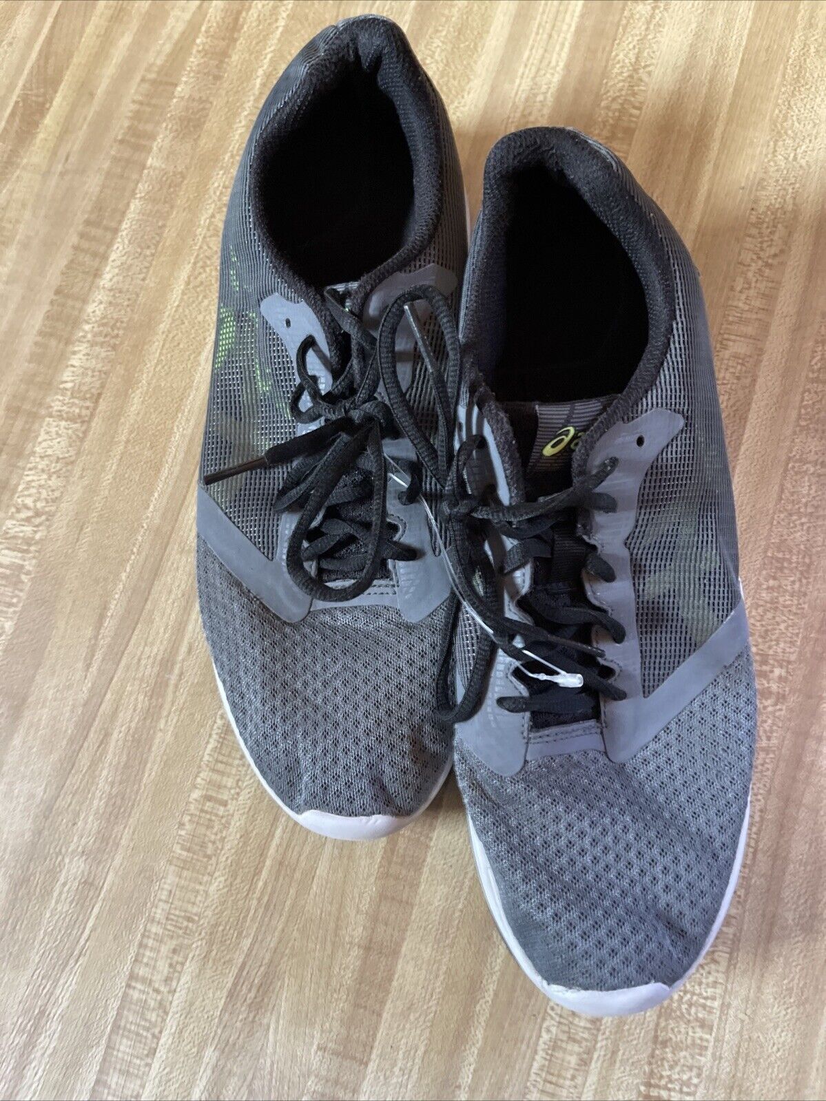 Pair of black and gray ASICS Patriot 10 men’s running shoes with mesh upper on wooden floor