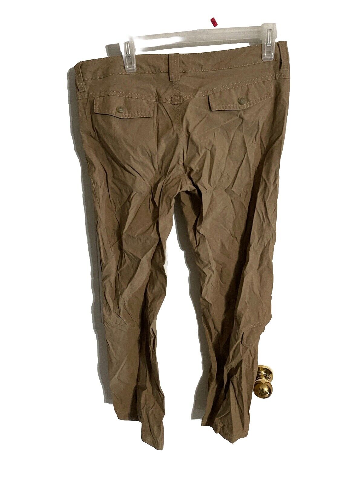 Athleta hiking pants petite in brown color hanging on clear hanger showing back pockets and fit