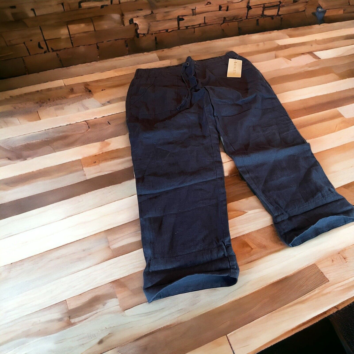 Black Athleta linen ankle pants laid flat on a wooden table with a tag attached