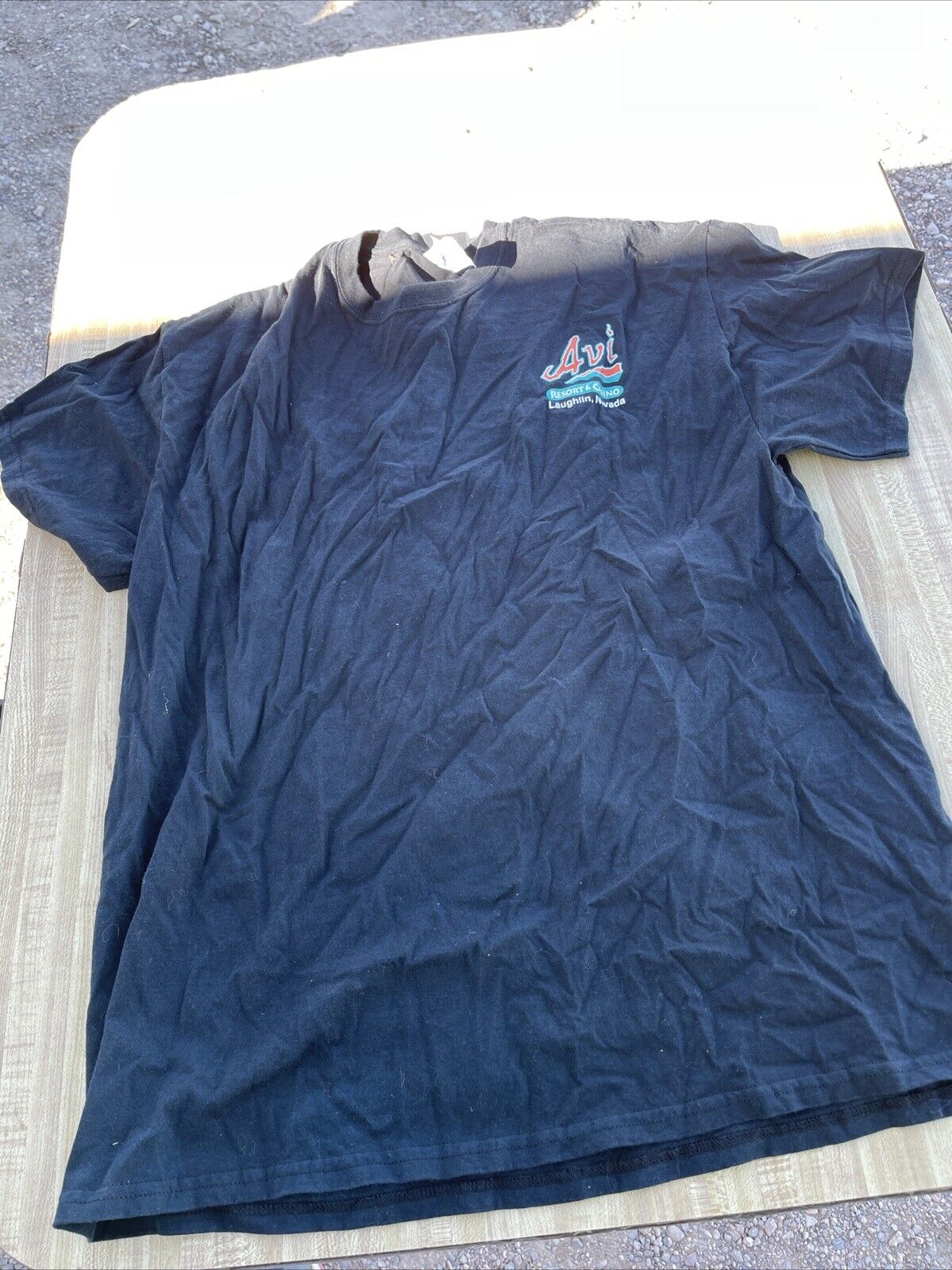 Wrinkled black Avi Casino t shirt XL with small logo on chest laid flat outdoors