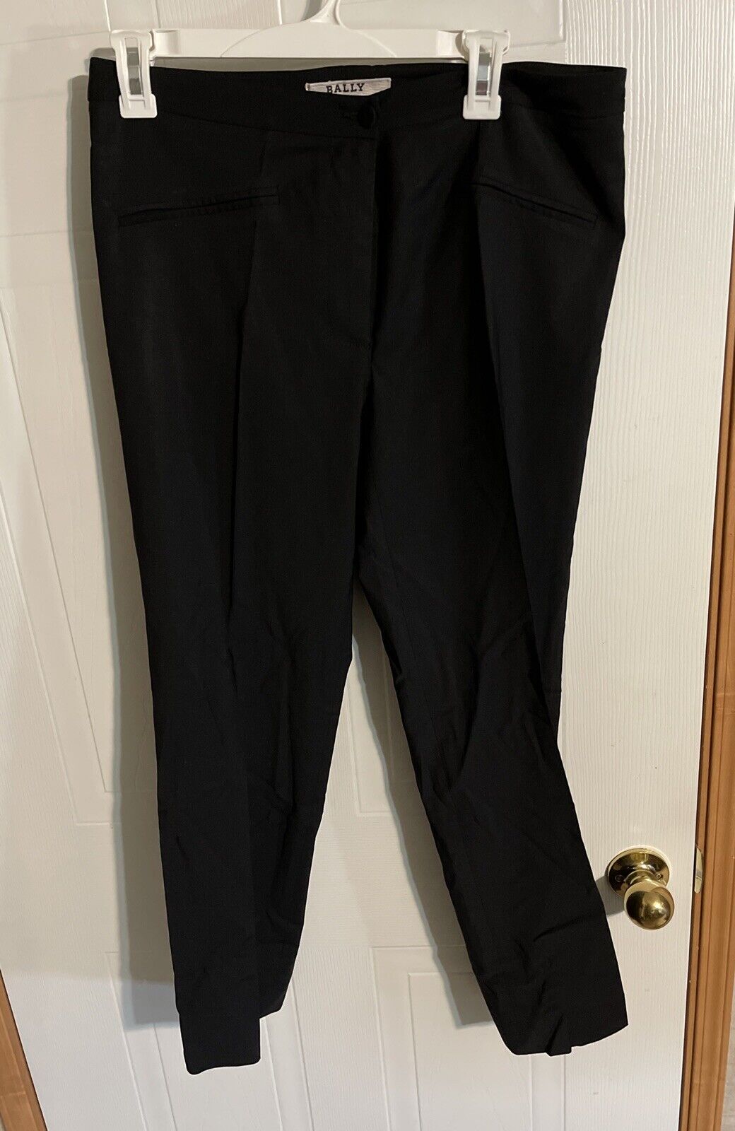 Bally black suit pants size 10 hanging on white hanger against white door background