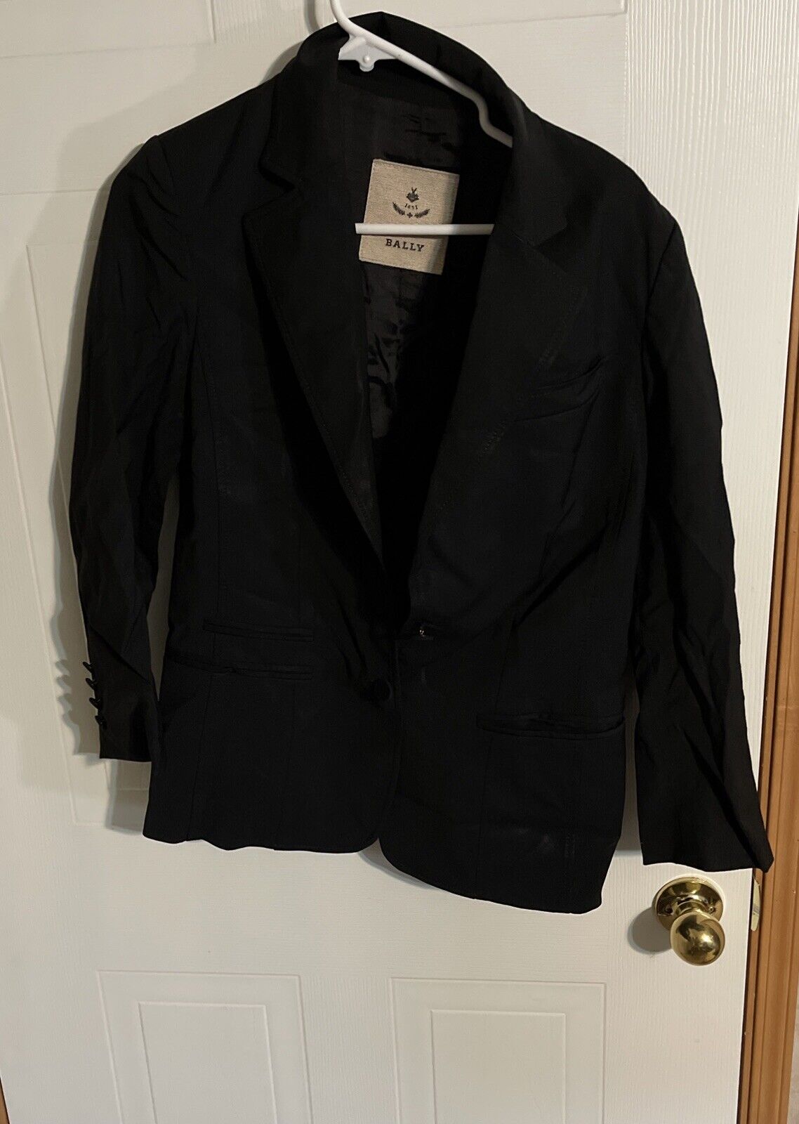 Bally women's black blazer hanging on white hanger with notch lapels and front pockets