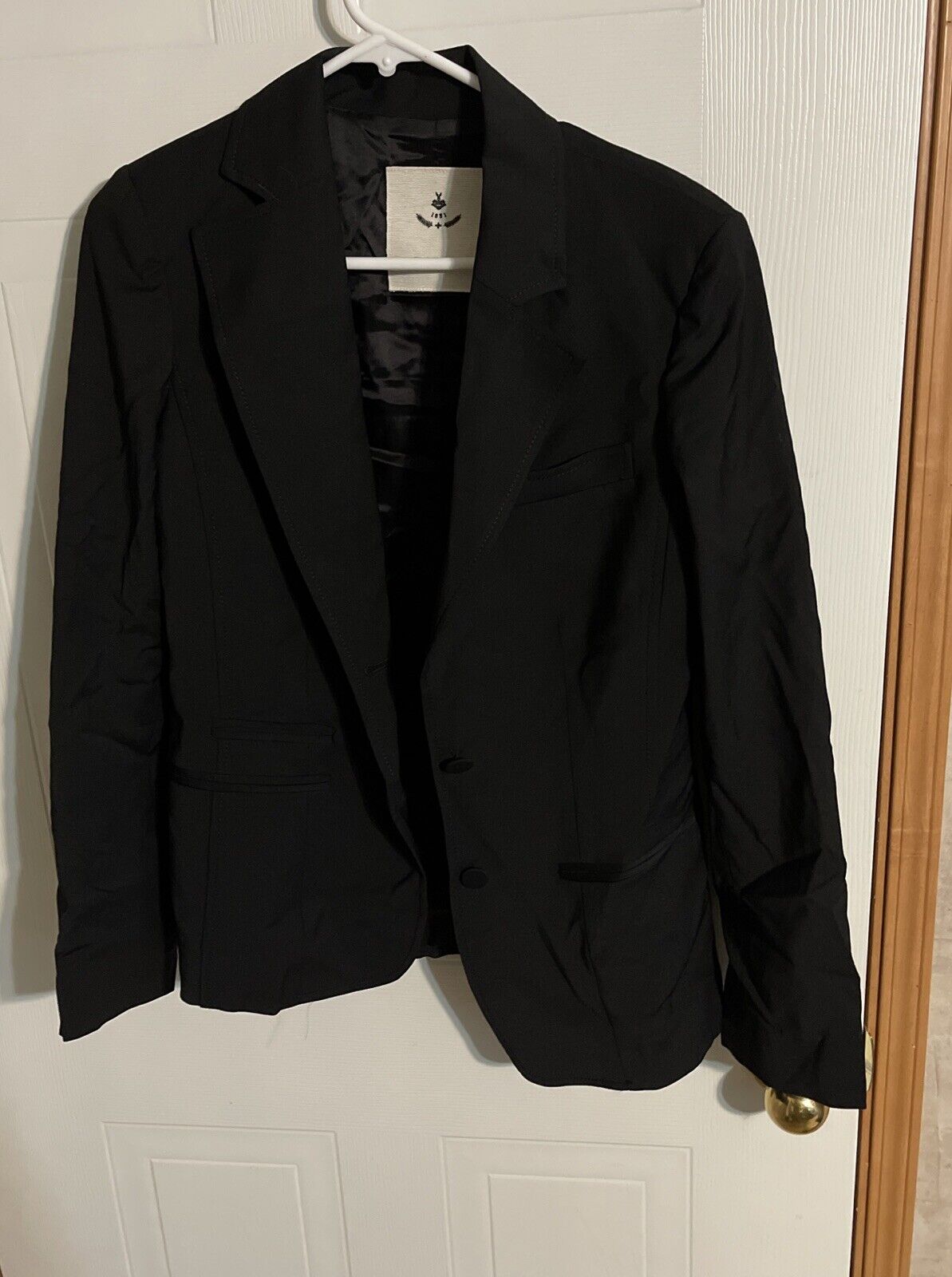 Bally women's black suit blazer hanging on white hanger on door with notch lapel