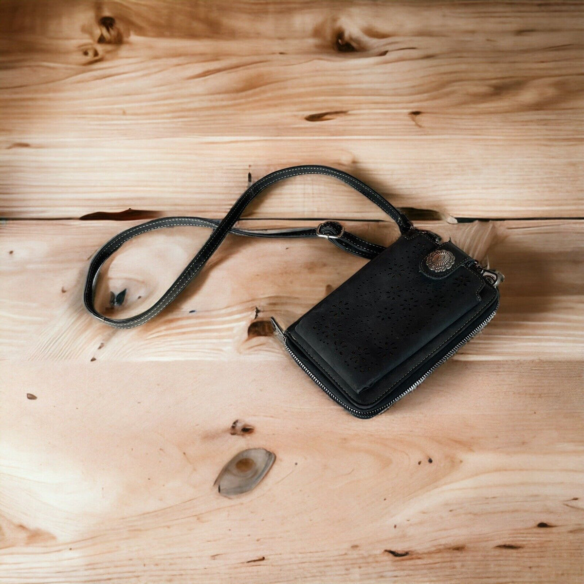 Black bling wallet with strap featuring perforated design and zipper on wooden surface