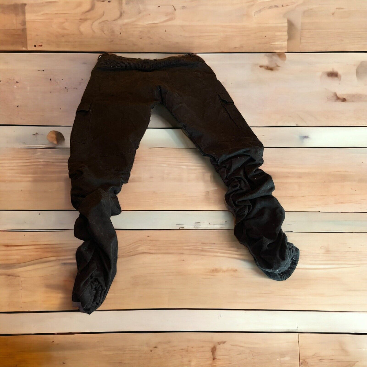 Black cargo pants with zipper pockets laid flat on wooden background from 1118 Emporium
