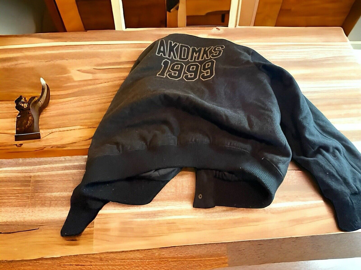 Black XXL hip hop fashion jacket with AKDMKS 1999 print laid on wooden table