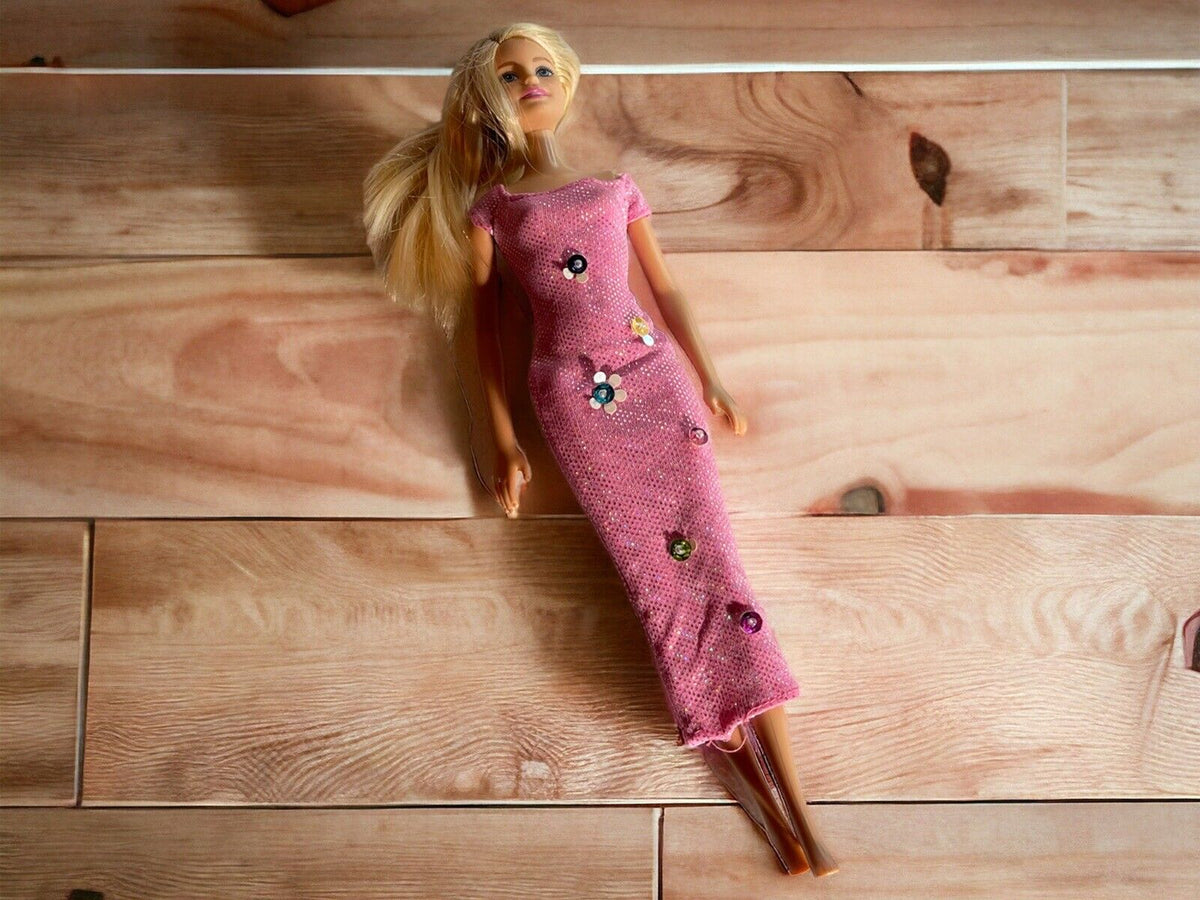 Classic Barbie doll in a long pink dress with floral embellishments lying on wooden floor