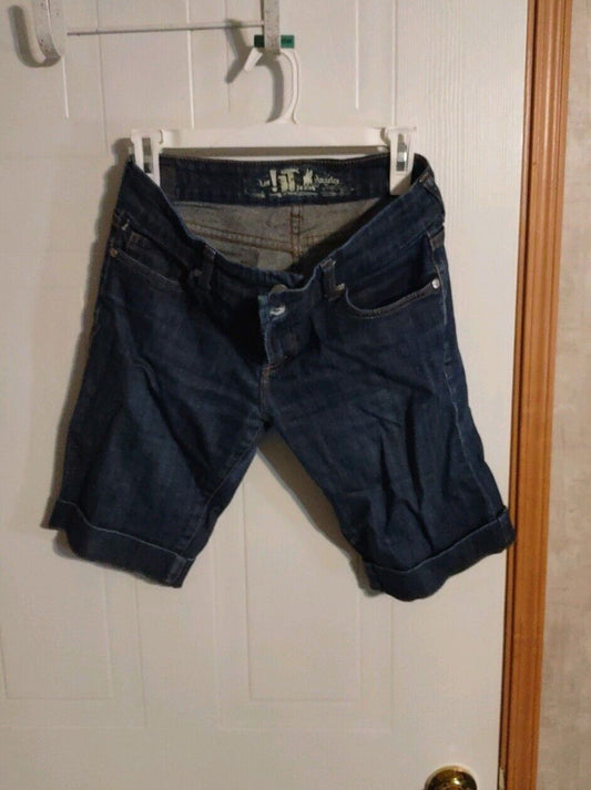 Dark denim size 28 Bermuda shorts hanging on white hanger against a white door background