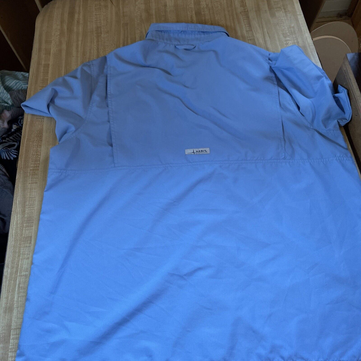 Back view of a light blue Habit vented fishing shirt XL laid flat on a wooden surface