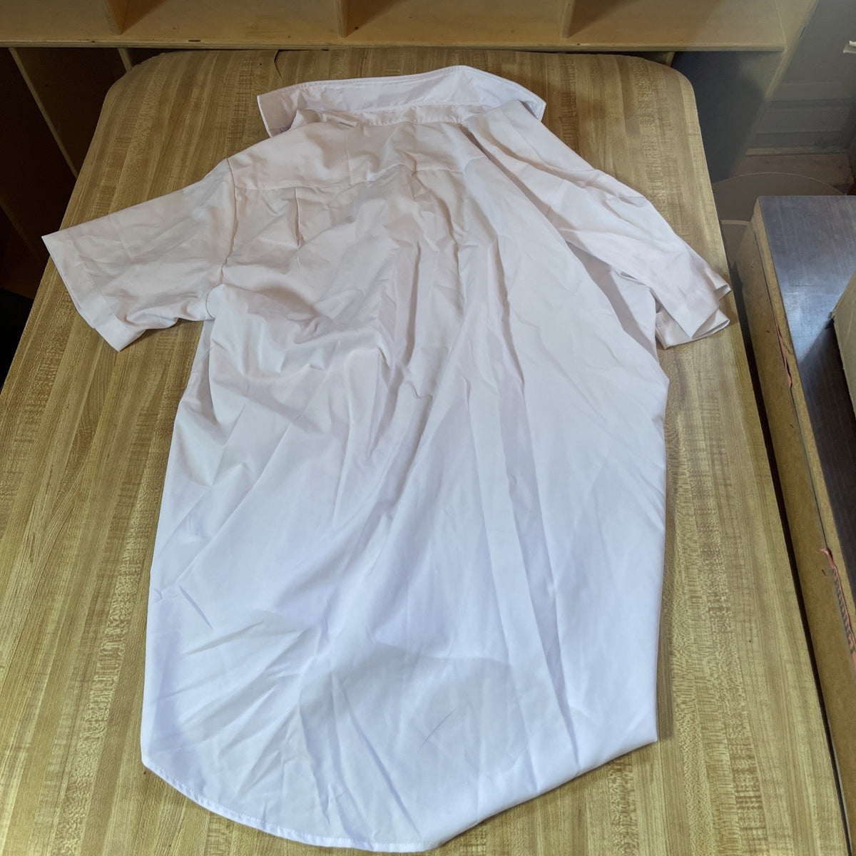 White men's athletic button up shirt laid flat on a wooden surface showing back side