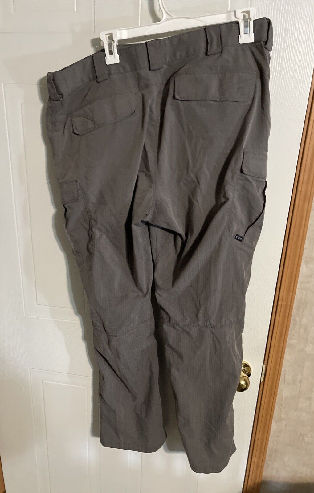 Men's tactical cargo pants in dark gray hanging on a hanger with multiple pockets from 1118 Emporium