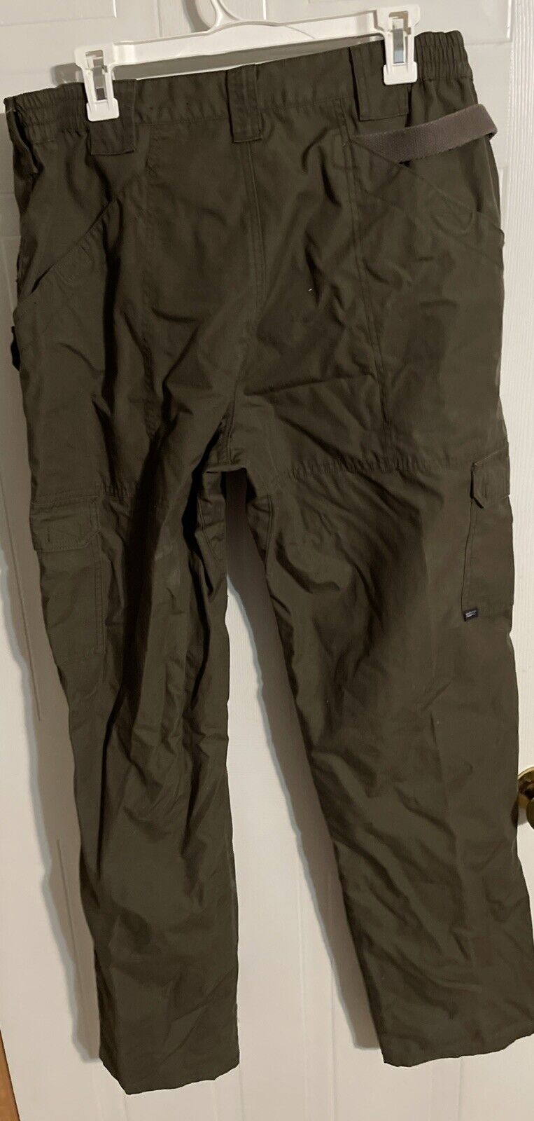 Olive green mens tactical cargo pants with multiple pockets hanging on a white hanger