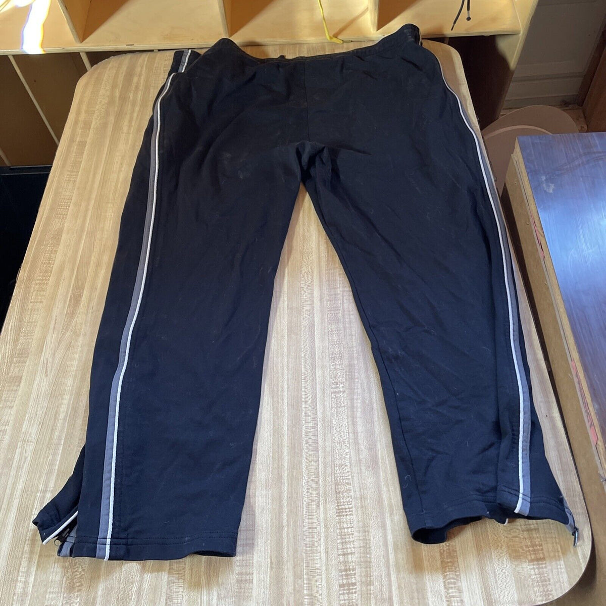 Reebok track pants XL in black with white side stripes laid flat on wooden surface