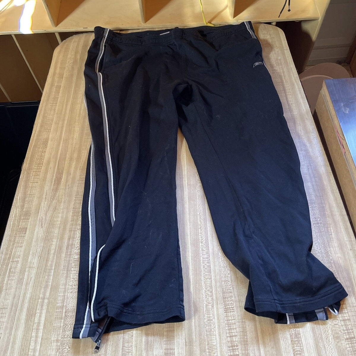 Black Reebok track pants XL with white side stripes laid flat on a wooden surface