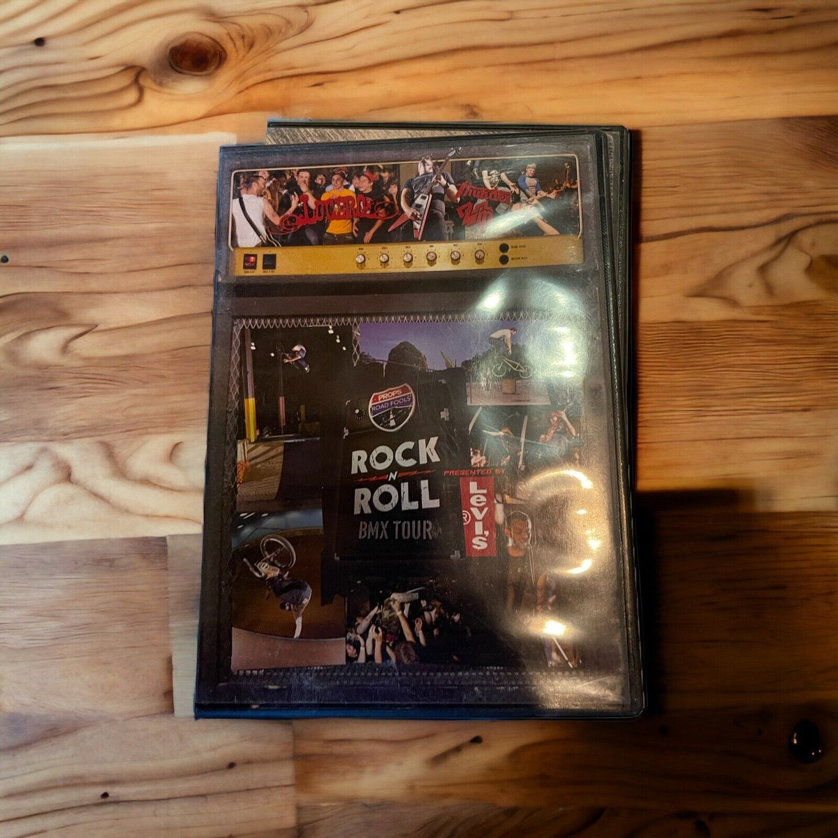 Stack of DVDs in plastic sleeves on wooden surface featuring rock and BMX images, not a monster truck dvd collection