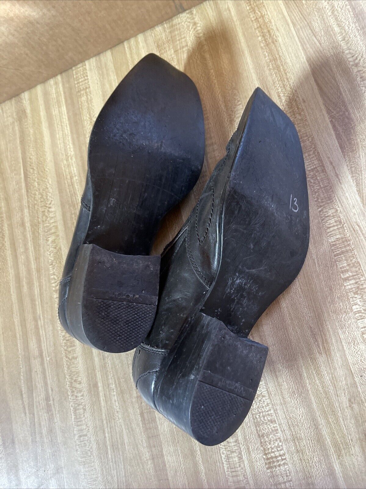 Bottom view of black Back Stage by Skechers shoes showing worn soles and heels on wooden floor
