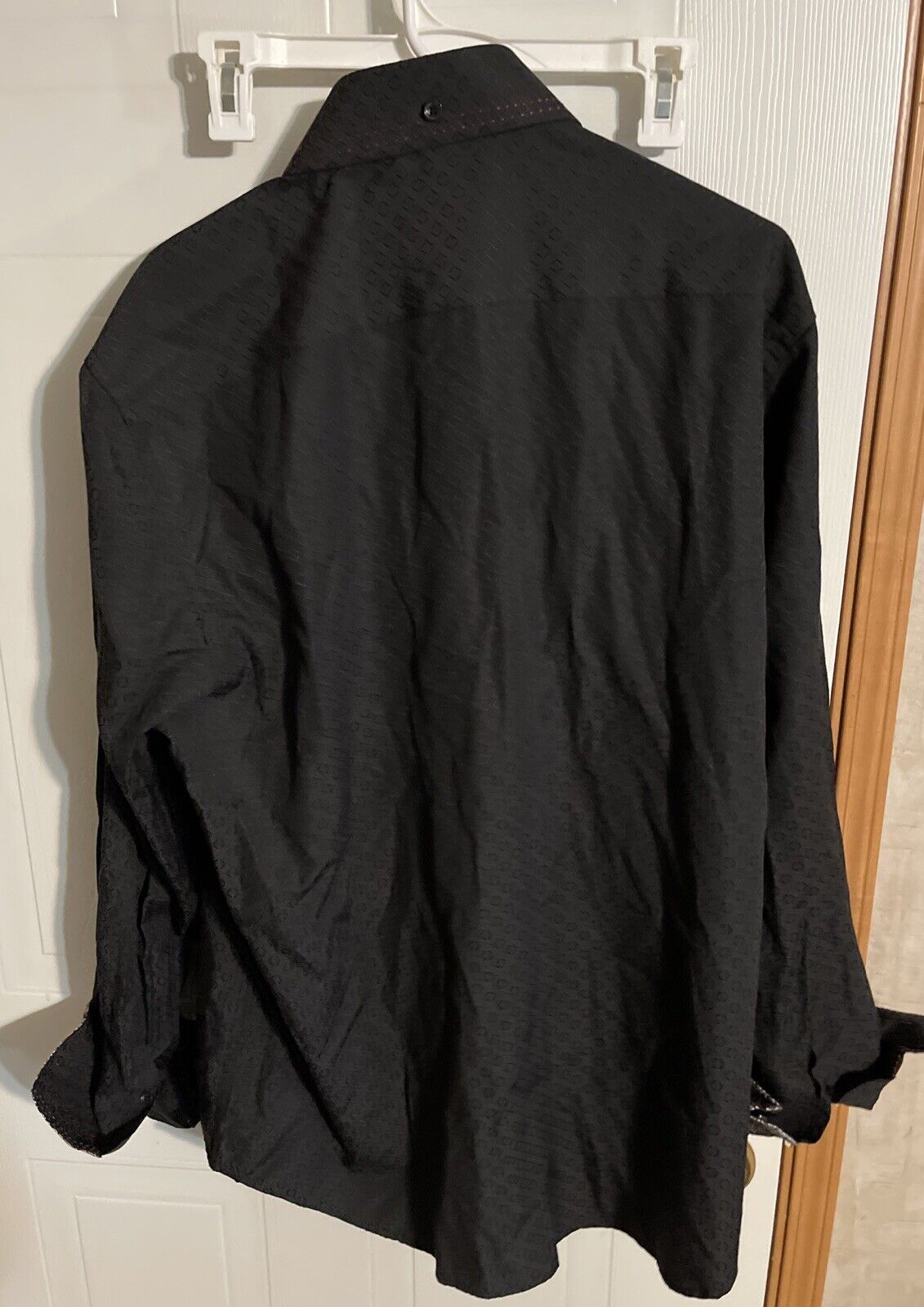 Black stylish button up shirt 2XL hanging on white hanger against a white door background