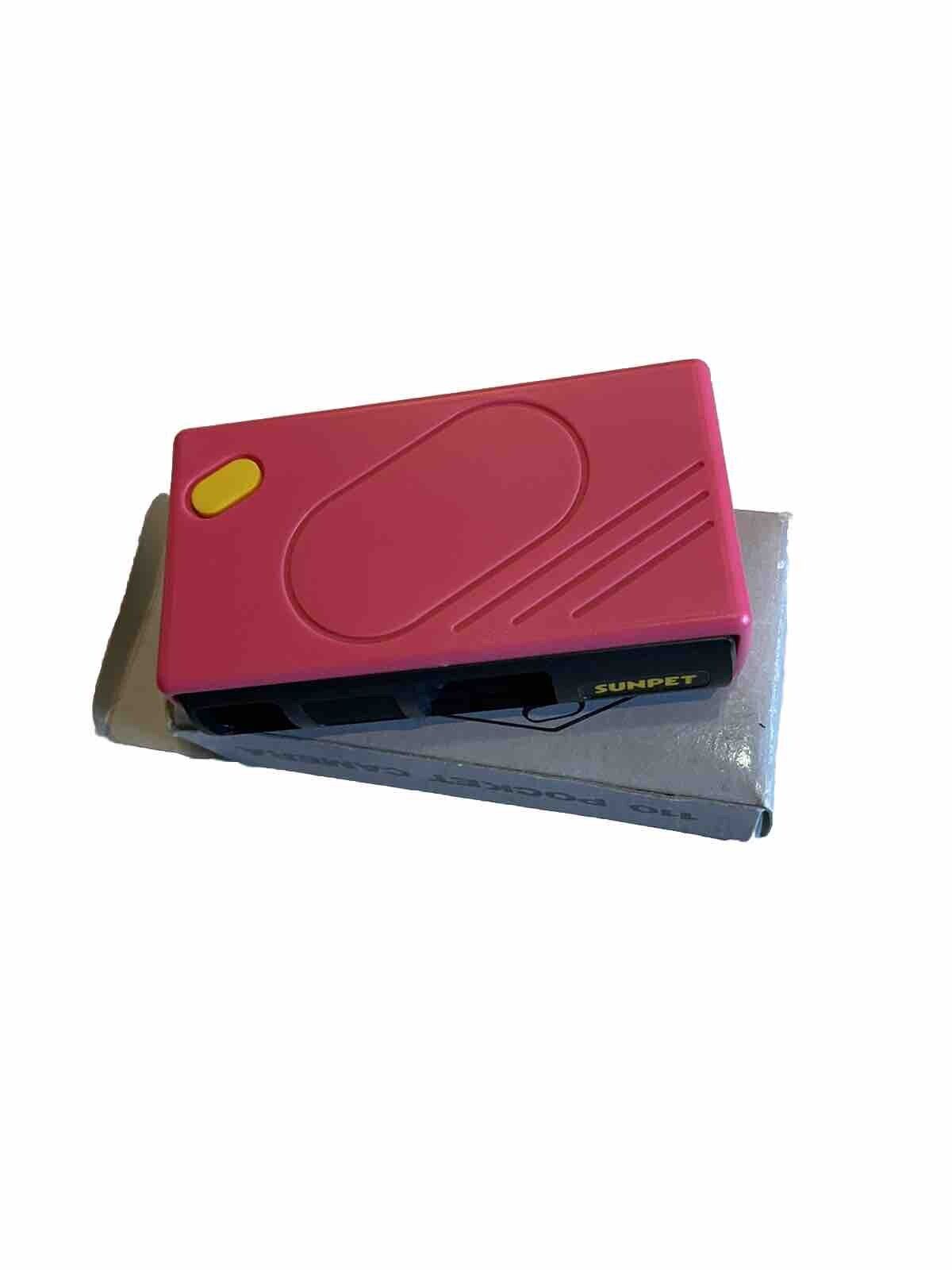 Bright pink 110 pocket camera with yellow shutter button resting on its original box