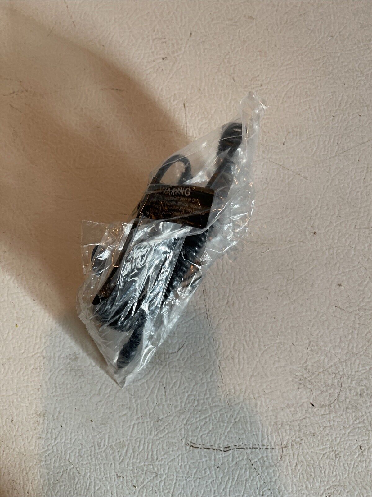 Universal DC power outlet 12v 24v cable adapter wrapped in clear plastic packaging on a textured surface