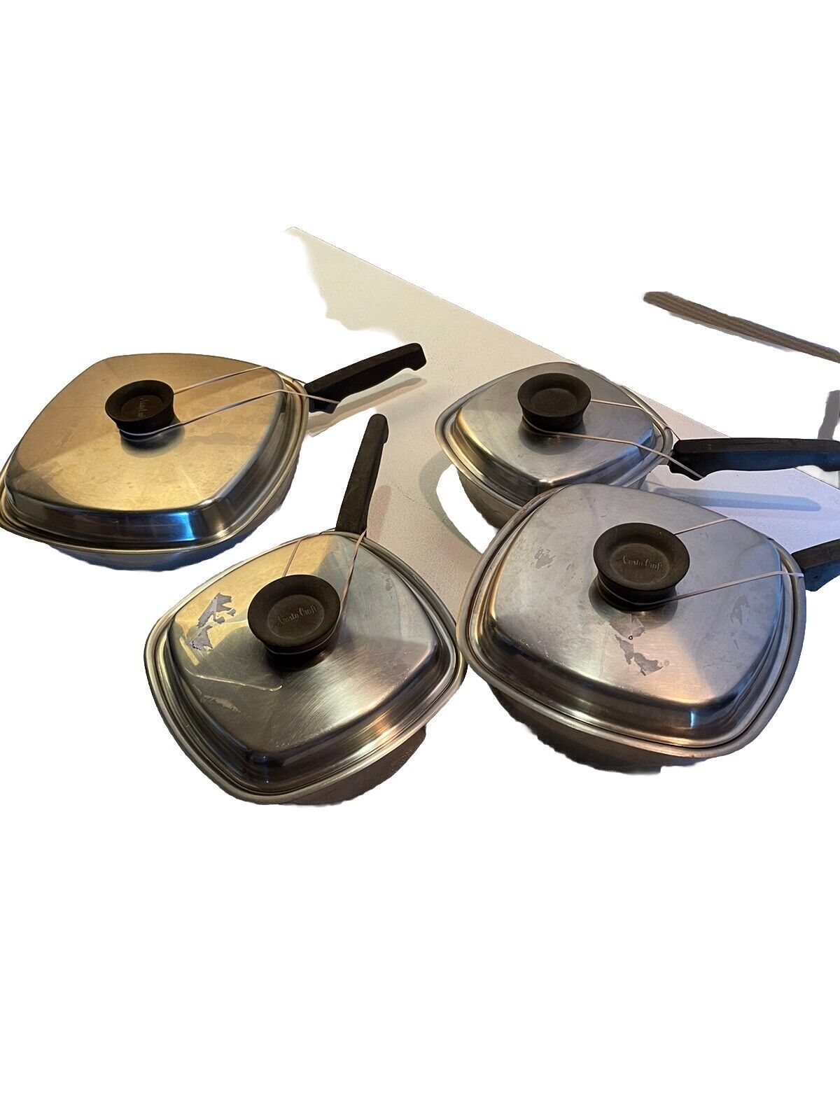Vintage stainless steel cookware set with four pots and black handles on white background
